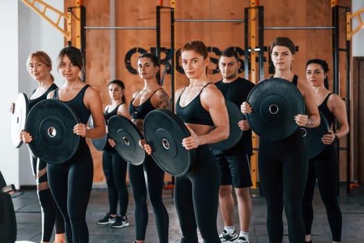 Holding weights. Group of young sportive people have crossfit day indoors in gym.