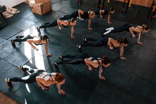 Using barbells. Group of young sportive people have crossfit day indoors in gym.