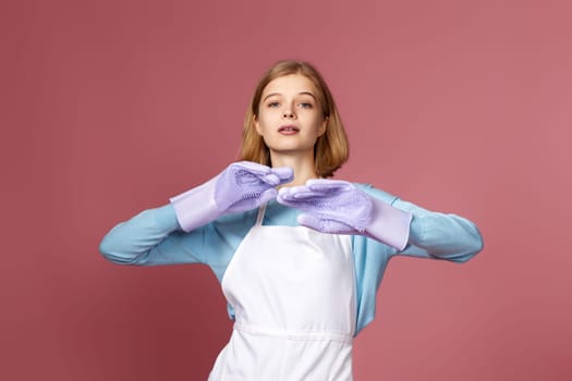 beautiful blonde lady in purple rubber gloves and cleaner apron on pink background.