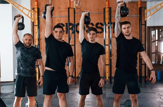 Lifting of heavy weights. Group of young sportive people have crossfit day indoors in gym.