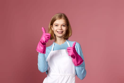 very excited blonde woman in pink rubber gloves and cleaner apron showing ok sign on pink background.