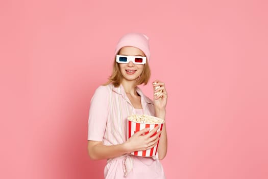 pretty blonde girl in pink t-shirt and hat holding bucket of popcorn isolated on pink background