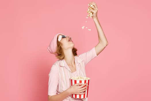 pleased blonde woman in t-shirt and hat eating popcorn on pink background.