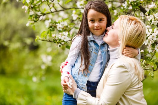 Little girl with her mother in blooming apple orchard on sunny spring day