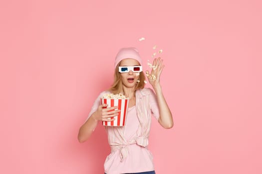 terrified girl with short haircut watching horror movie , holding bucket of popcorn on pink background