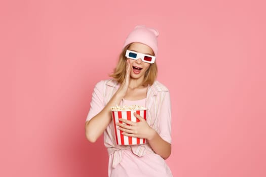 amazed woman in 3d glasses holding bucket of popcorn on pink background