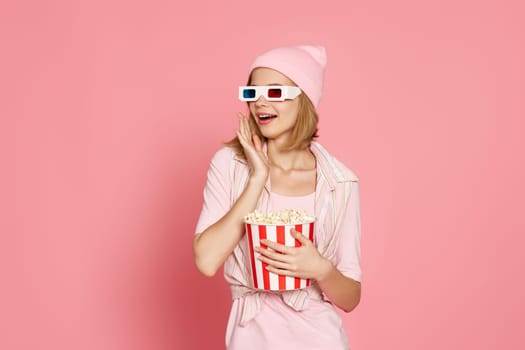 amazed woman watching movie film, holding bucket of popcorn on pink background
