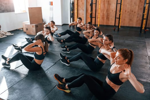 Doing abs. Group of young sportive people have crossfit day indoors in gym.
