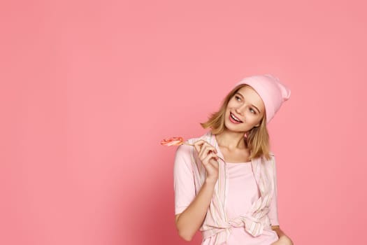 beautiful blonde woman holding candy on pink background. copy space