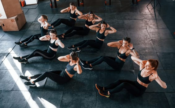 Doing abs. Group of young sportive people have crossfit day indoors in gym.