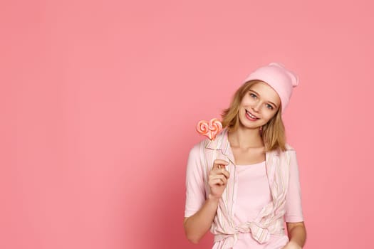 beautiful blonde woman holding big heart lollipop on pink background. copy space