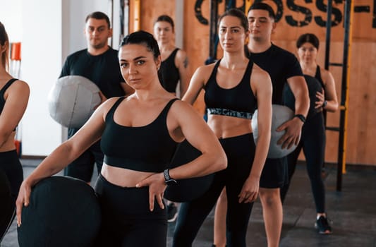 With fitness balls. Group of young sportive people have crossfit day indoors in gym.