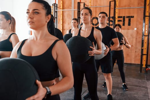 With fitness balls. Group of young sportive people have crossfit day indoors in gym.
