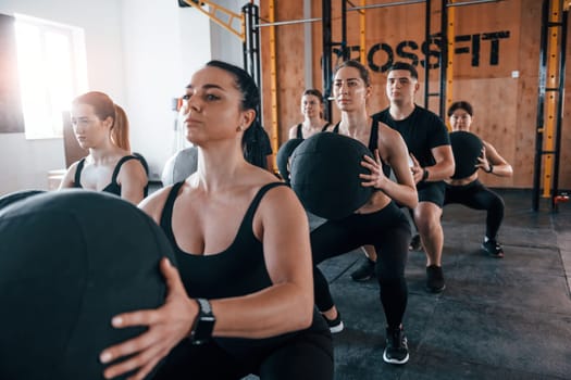 With fitness balls. Group of young sportive people have crossfit day indoors in gym.