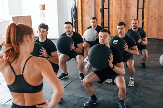 With fitness balls. Group of young sportive people have crossfit day indoors in gym.