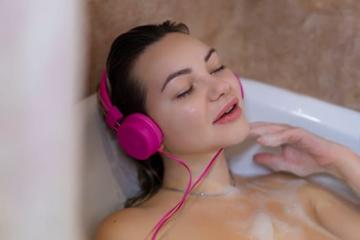 Beautiful young woman with headphones relaxing in bathtub.