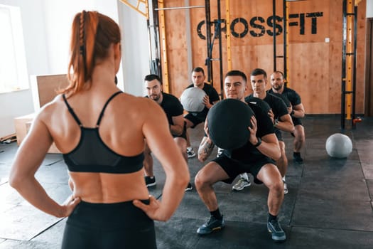 With fitness balls. Group of young sportive people have crossfit day indoors in gym.