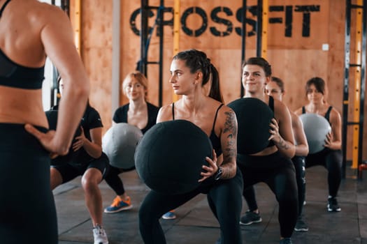 With fitness balls. Group of young sportive people have crossfit day indoors in gym.