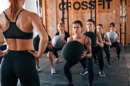 With fitness balls. Group of young sportive people have crossfit day indoors in gym.