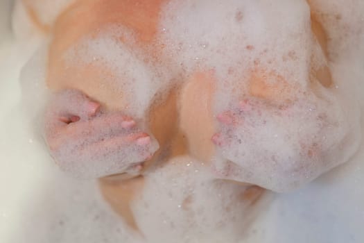 A sexy girl takes a bath. Large beautiful female breasts in bath foam.