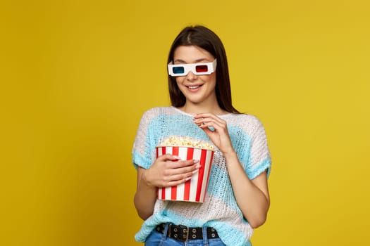 beautiful brunette girl in blue pullover eating popcorn isolated on yellow background