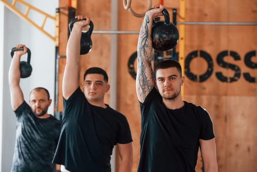 By using heavy weights. Group of young sportive people have crossfit day indoors in gym.