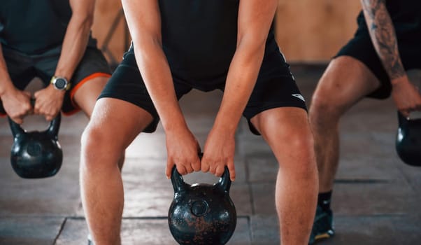By using heavy weights. Group of young sportive people have crossfit day indoors in gym.