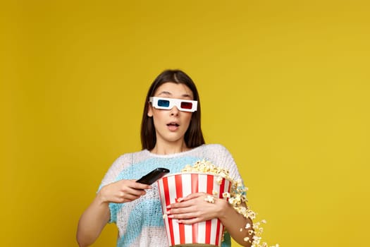 pretty woman with remote control holding bucket of popcorn and jumping on yellow background.