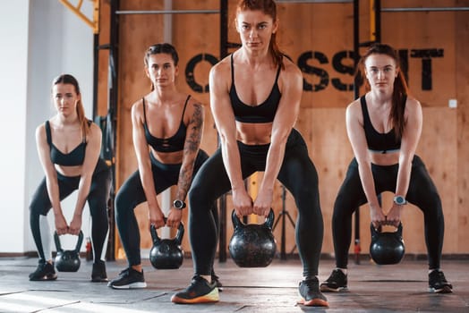 By using heavy weights. Group of young sportive people have crossfit day indoors in gym.