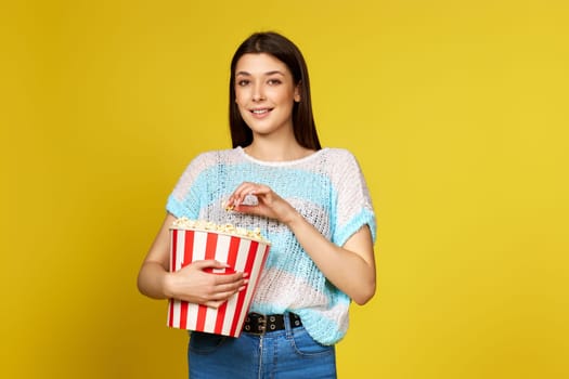 beautiful brunette girl in blue pullover eating popcorn isolated on yellow background