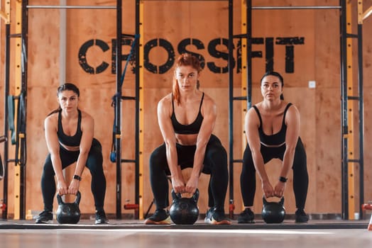 Using barbells. Group of young sportive people have crossfit day indoors in gym.