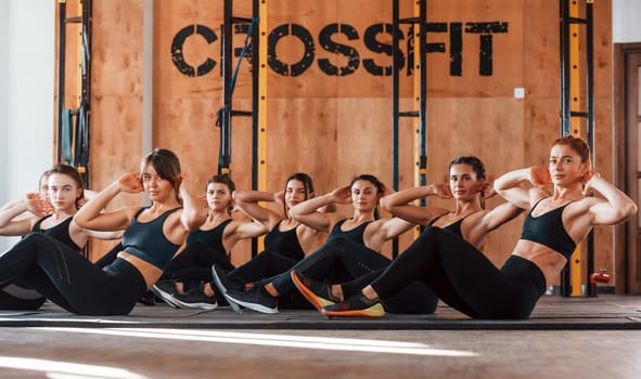 Doing abs. Group of young sportive people have crossfit day indoors in gym.