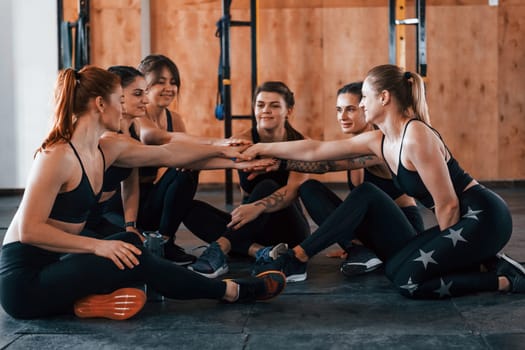 Sitting on floor. Group of young sportive people have crossfit day indoors in gym.