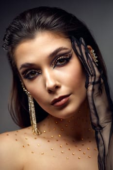 beauty fashionable model woman with creative eye makeup with arrows and rhinestones in long earring on gray background