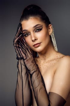 beauty fashionable model woman with creative eye makeup with arrows and rhinestones in long earring on gray background