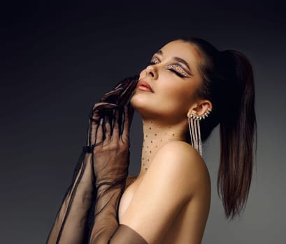 beauty fashionable model woman with creative eye makeup with arrows and rhinestones in long earring on gray background