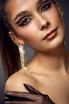 beauty fashionable model woman with creative eye makeup with arrows and rhinestones in long earring on gray background