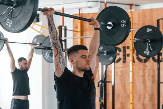 Lifting barbell. Group of young sportive people have crossfit day indoors in gym.
