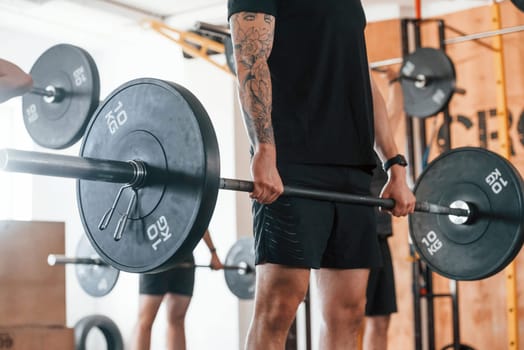 Lifting barbell. Group of young sportive people have crossfit day indoors in gym.