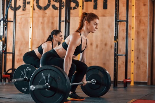Lifting barbell. Group of young sportive people have crossfit day indoors in gym.
