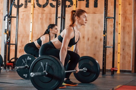 Lifting barbell. Group of young sportive people have crossfit day indoors in gym.