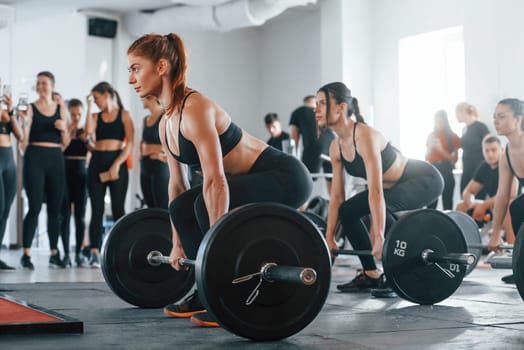 Lifting barbell. Group of young sportive people have crossfit day indoors in gym.