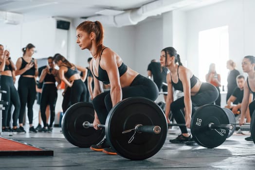 Lifting barbell. Group of young sportive people have crossfit day indoors in gym.