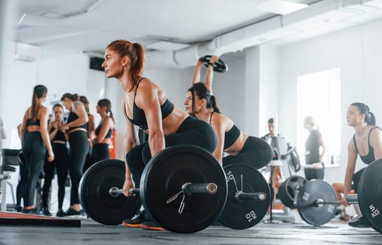 Lifting barbell. Group of young sportive people have crossfit day indoors in gym.