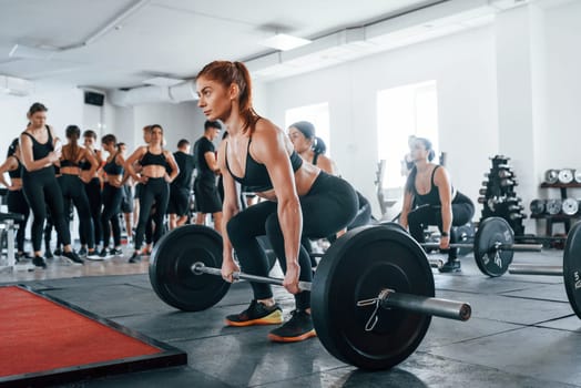 Lifting barbell. Group of young sportive people have crossfit day indoors in gym.