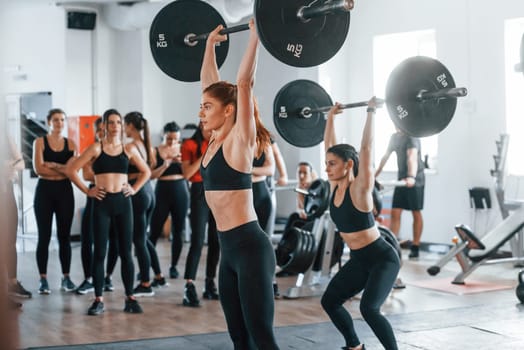 Lifting barbell. Group of young sportive people have crossfit day indoors in gym.