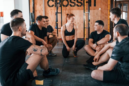 Taking a break. Group of young sportive people have crossfit day indoors in gym.