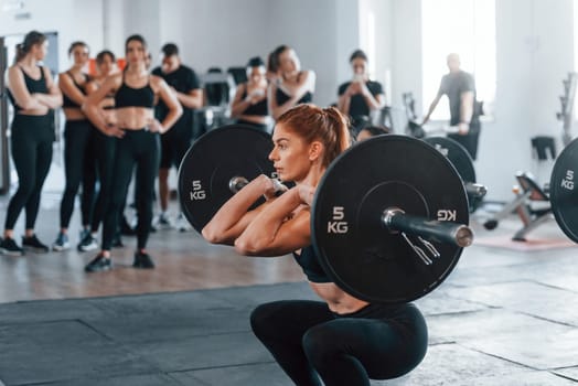 Lifting barbell. Group of young sportive people have crossfit day indoors in gym.