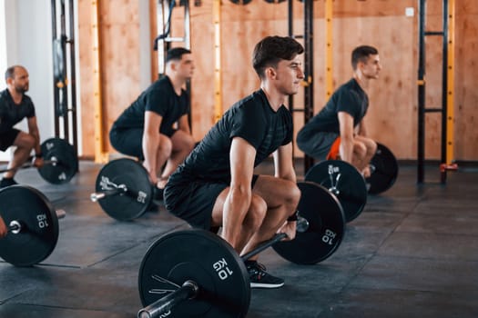 Busy by doing exercises. Group of young sportive people have crossfit day indoors in gym.