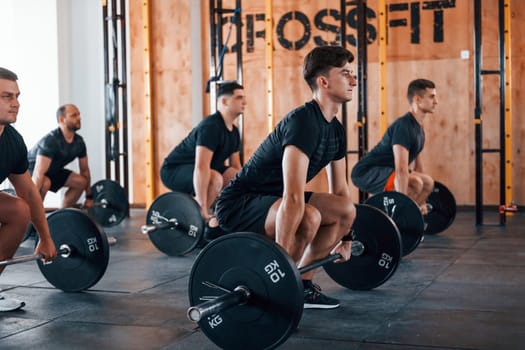 Busy by doing exercises. Group of young sportive people have crossfit day indoors in gym.